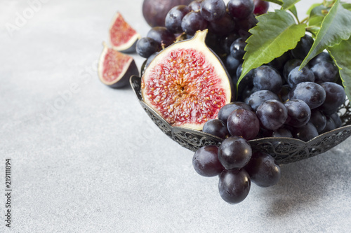 Fresh figs and black grapes with leaves in a plate on a grey table selective focus. Copy space