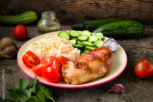 Grilled chicken leg, white rice, slised cucumber with sesame seeds, tomtoes and herbs. photo