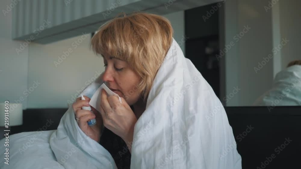 A woman lying on a bed uses a drop in her nose to treat a cold as prescribed by a doctor A woman lying on a bed uses a drop in her nose to treat a cold as prescribed by a doctor