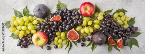 Banner of fresh autumn fruits. Grapes black and green  figs and leaves on a grey table.