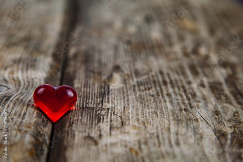 Red glass heart on an old wooden background. Romantic background.