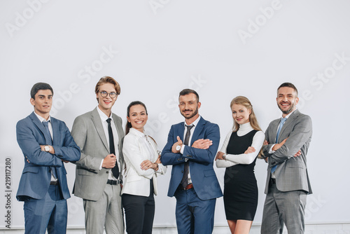 smiling businesspeople with crossed arms posing near board after training in hub