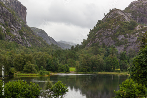 Mountain slopes and forest reflect in the water of mountain lake in the green valley at murky day in Rogaland country, Norway