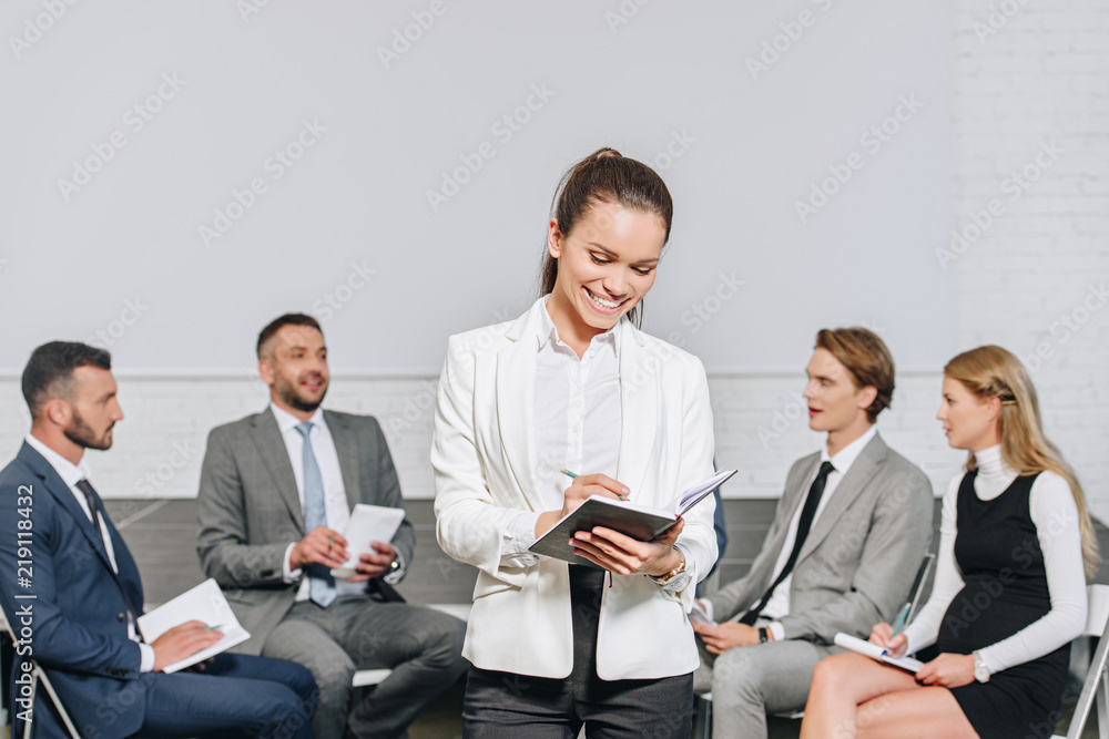 business coach writing something to notebook in front of businesspeople at training in hub business coach writing something to notebook in front of businesspeople at training in hub
