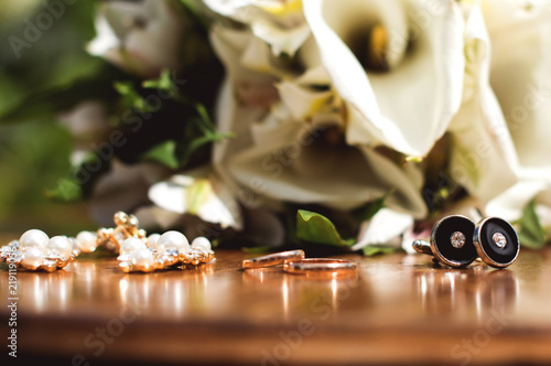 toned picture with wedding rings lie on a wooden surface against the background of a bouquet of flowers