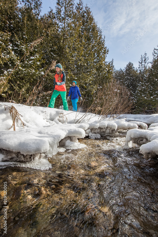 Pair of female friends snowshoeing in forest.