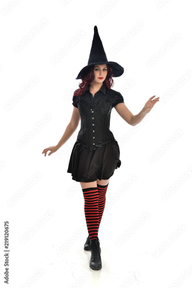 full length portrait of red haired girl wearing black witch costume and pointy hat. standing pose, isolated on white studio background. full length portrait of red haired girl wearing black witch costume and pointy hat. standing pose, isolated on white studio background.