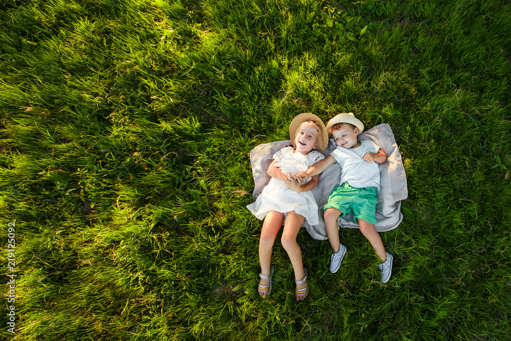 A boy and a girl are lying on the green grass. Top view. Space for text.