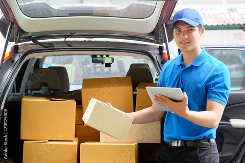 Portrait of a delivery Asian man standing in front of his van while using tablet for checking a package