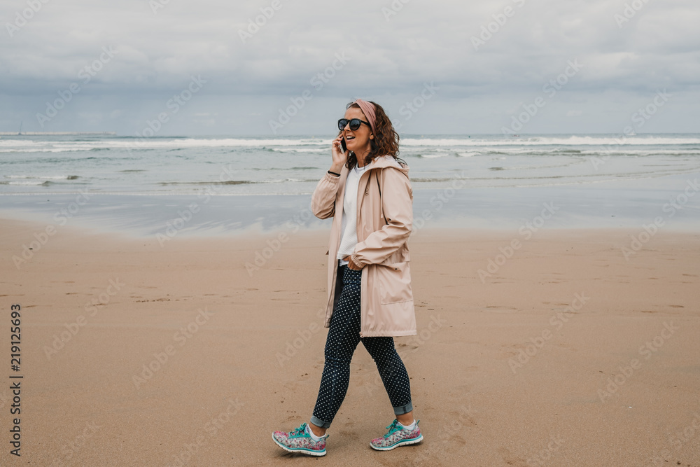 .Young and cheerful girl walking through a huge beach in northern Spain, in Asturias. Taking pictures and talking on his smartphone on a cloudy summer day. Enjoying relaxed and at peace. Lifestyle. .Young and cheerful girl walking through a huge beach in northern Spain, in Asturias. Taking pictures and talking on his smartphone on a cloudy summer day. Enjoying relaxed and at peace. Lifestyle.