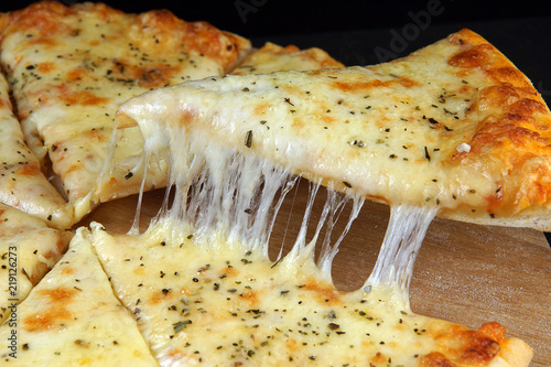 Hot appetizing cheese pizza, cut into pieces, one of which is picked up