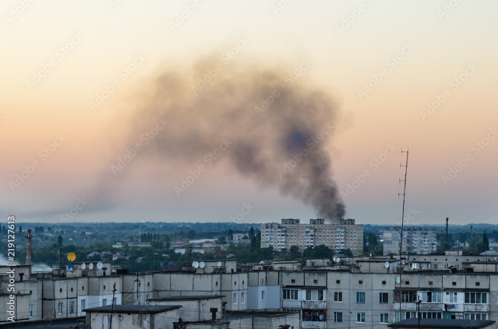 Fire in the city in a high-rise building, black smoke over houses in the evening