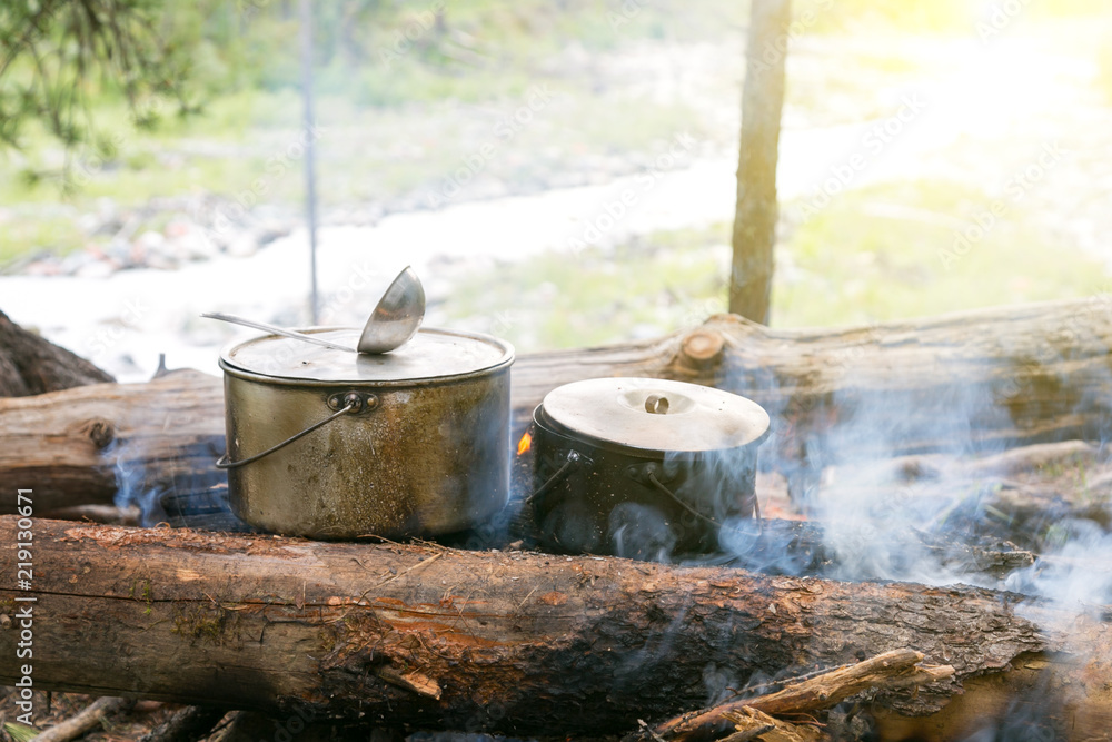 Two pots stand on the fire in the forest. Preparation of food in the trek, two iron pots are heated on an open fire. Two pots stand on the fire in the forest. Preparation of food in the trek, two iron pots are heated on an open fire.