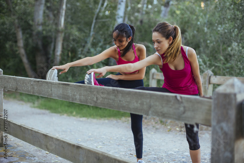 Two active women stretching at a brick wall