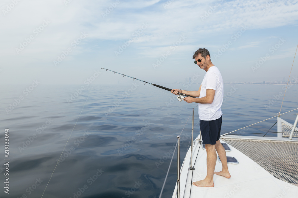 Mature man standing on catamaran, fishing Mature man standing on catamaran, fishing