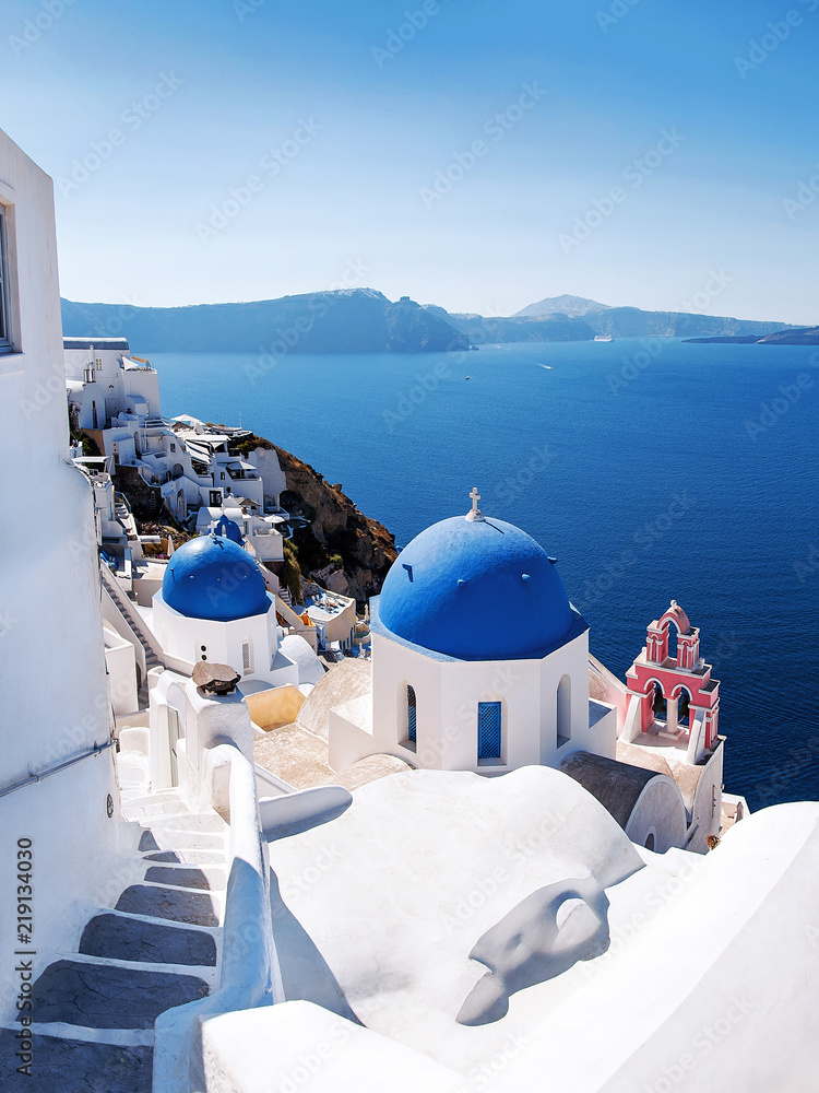Naklejka premium View with Greek orthodox church with blue domes and sea in Oia in Santorini, Greece, Europe. Beautiful scenery above the caldera overlooking the Aegean Sea.