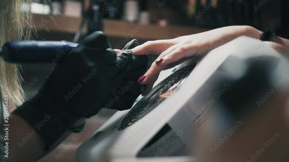 Closeup beautician in black gloves removes lacque off female's nail in a nail salon. Professional manicure in beauty salon Closeup beautician in black gloves removes lacque off female's nail in a nail salon. Professional manicure in beauty salon