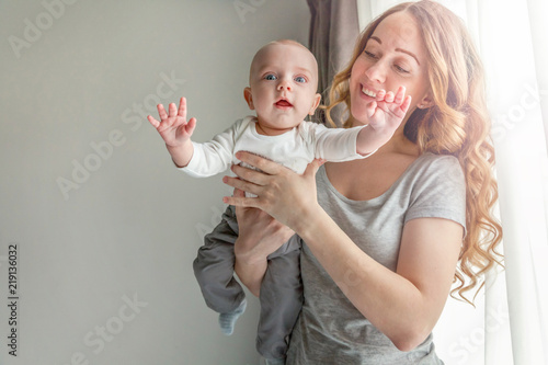 Young mother holding newborn child. Woman and infant boy relax and playing in bedroom near windiow. Mom of breast feeding baby. Family, maternity, tenderness, parenthood, responsibility concept photo