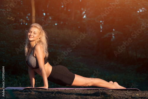 young beautiful female practicing ashtanga yoga in green park;