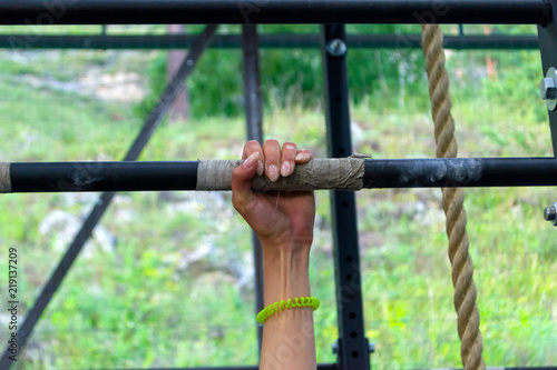 hand girl with a manicure on an iron bar with tense veins and muscles against the background of a rope and greenery in the open air. The power of women.