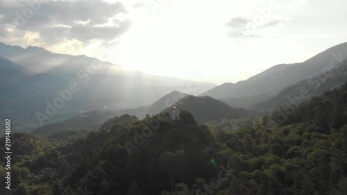 Aerial: flying over valley and green forest, rural village and old chapel perched on top, Susa Valley, the Alps, Turin, Italy. Native Cinelike D-Log ungraded flat color profile.