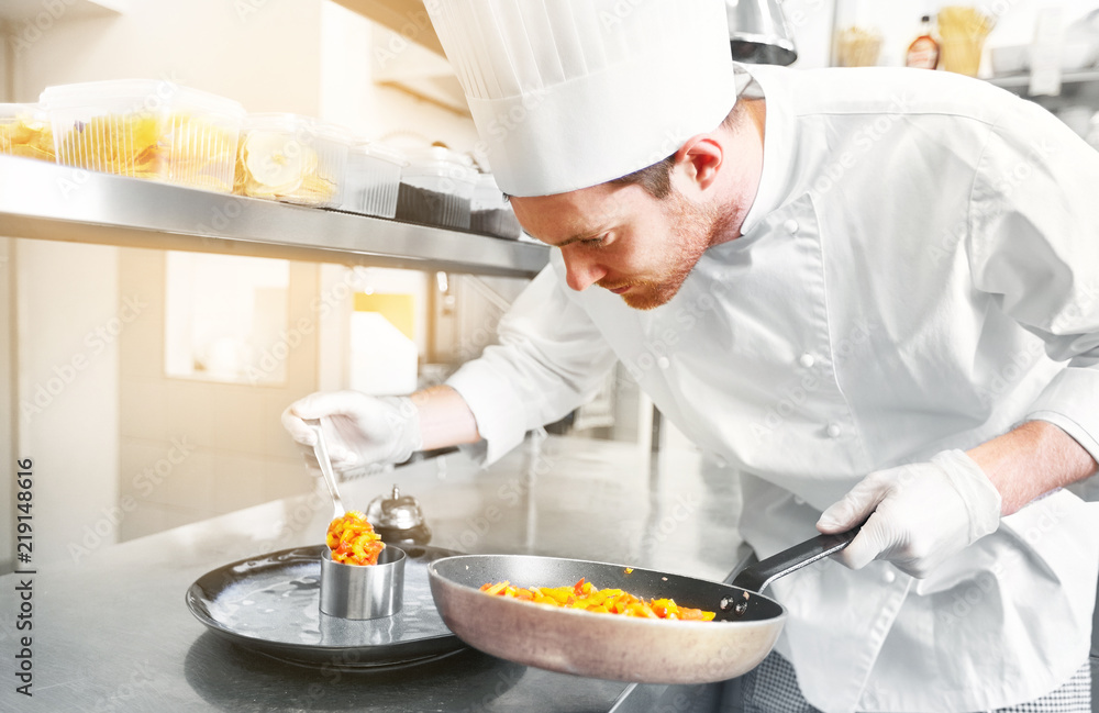 food cooking, profession and people concept - happy male chef cook with frying pan and mold serving stewed vegetables on plate at restaurant kitchen