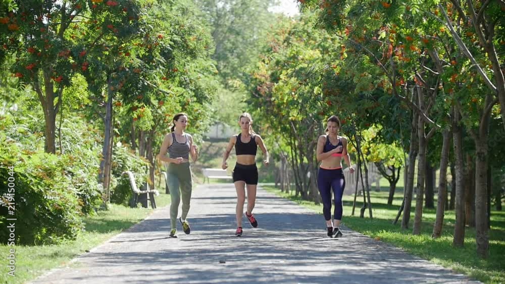 Three young girls are running in the Park among the green trees Three young girls are running in the Park among the green trees