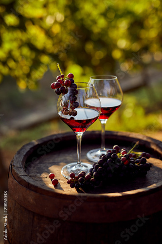 Two glasses of red wine with a bottle on a wooden barrel