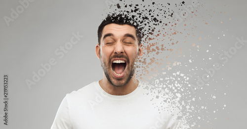 emotions, stress and people concept - crazy shouting man in t-shirt over gray background with particle dispersion effect