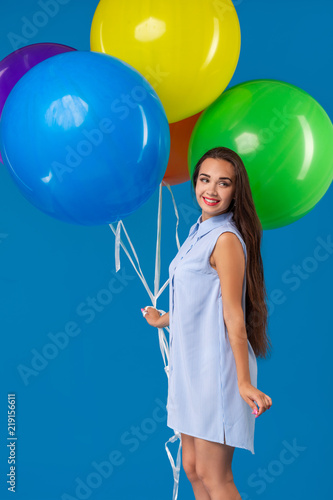 Smiling young woman looking camera and holding colorful air balloons isolated over blue © nazarovsergey