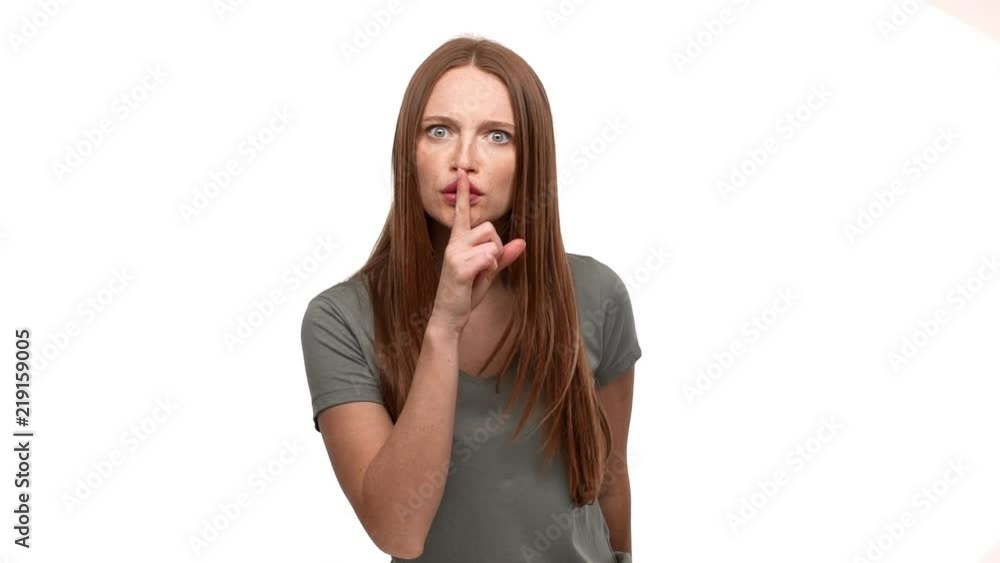 Portrait of persistent strict woman 20s holding index finger on lips and asking to keep quiet, isolated over white background slow motion. Concept of emotions Portrait of persistent strict woman 20s holding index finger on lips and asking to keep quiet, isolated over white background slow motion. Concept of emotions