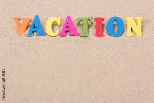 Word vacations of colored wooden letters on sandy