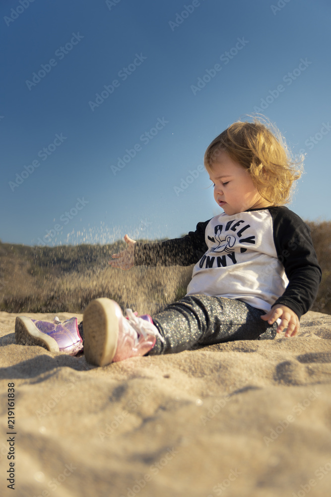 Beautiful little girl playing with sand on the beach in Cordoba, Argentina, during a sunny winter afternoon Beautiful little girl playing with sand on the beach in Cordoba, Argentina, during a sunny winter afternoon