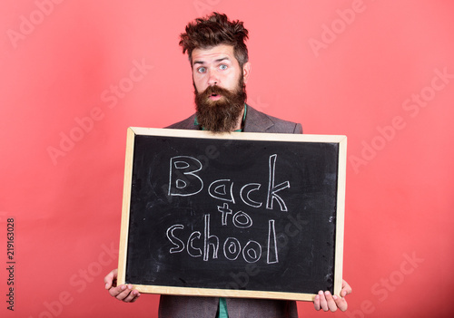 Teacher informs back to studying, begin school year. Teacher or bearded educator stands and holds blackboard with inscription back to school red background. School and teacher wait for you