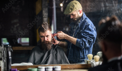 Barber with clipper trimming hair on nape of client. Hipster lifestyle concept. Hipster client getting haircut. Barber with hair clipper works on haircut of bearded guy barbershop background