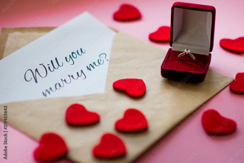 Beautiful wedding ring with precious stone in a red gift box, carved hearts  and envelope with a note "Will you marry me?" on pink background. Marriage  proposal concept. Stock Photo | Adobe