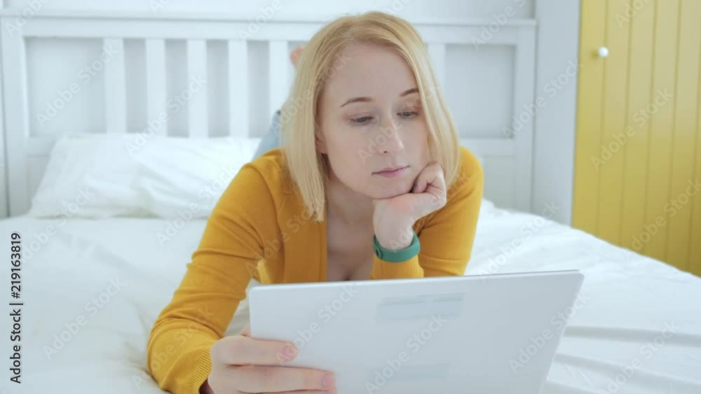 Beautiful blonde Caucasian woman using digital tablet PC while lying on the bed Beautiful blonde Caucasian woman using digital tablet PC while lying on the bed