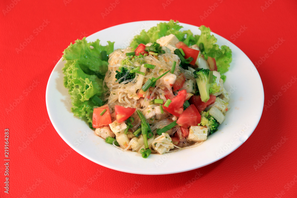 Cellophane noodles salad with Vietnamese Pork Sausage and variety vegetable such as lettuce, tomato and onion in the round plate on the red floor. Cellophane noodles salad with Vietnamese Pork Sausage and variety vegetable such as lettuce, tomato and onion in the round plate on the red floor.