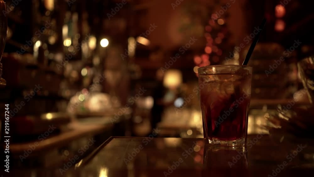 Glass of alcoholic beverage standing of a table in an Italian bar. Blurred background with a bartender. Concept of alcohol consumption and addiction. Locked down real time establishing shot Glass of alcoholic beverage standing of a table in an Italian bar. Blurred background with a bartender. Concept of alcohol consumption and addiction. Locked down real time establishing shot