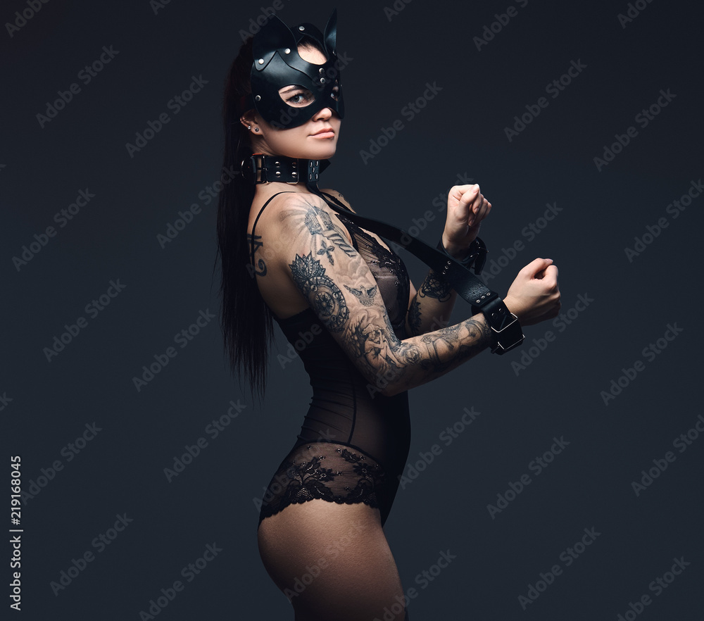 Sexy woman wearing black lingerie in BDSM cat leather mask and accessories posing on dark background. 