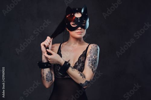 Sexy woman wearing black lingerie in BDSM cat leather mask and accessories posing on dark background.  © Fxquadro