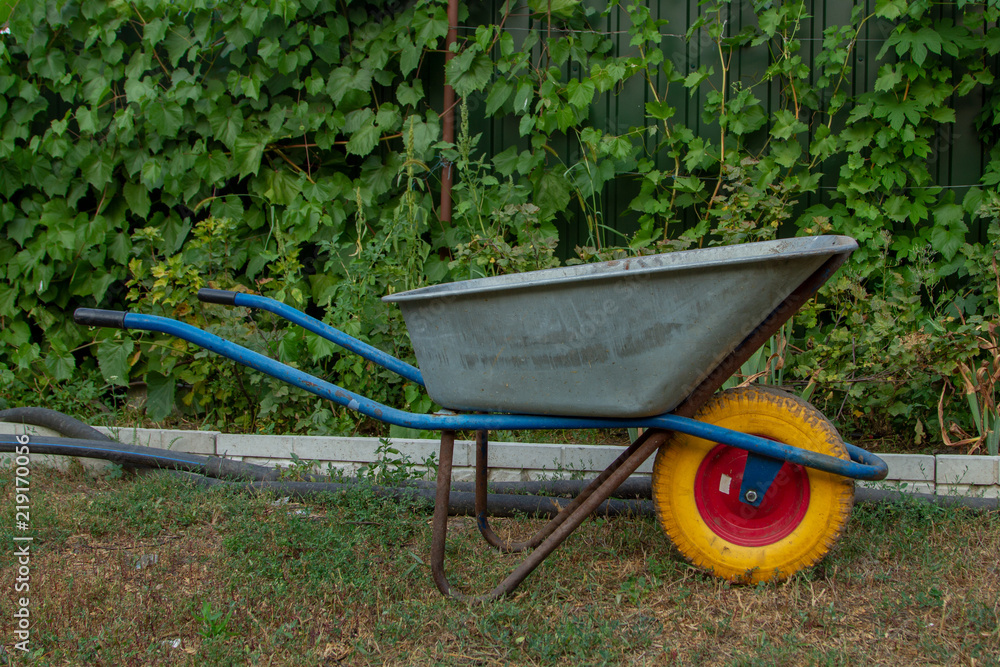 A metal wheelbarrow with a yellow wheel for home and garden. A wheelbarrow with blue handles and a yellow wheel. Construction cart for the household. A metal wheelbarrow with a yellow wheel for home and garden. A wheelbarrow with blue handles and a yellow wheel. Construction cart for the household.