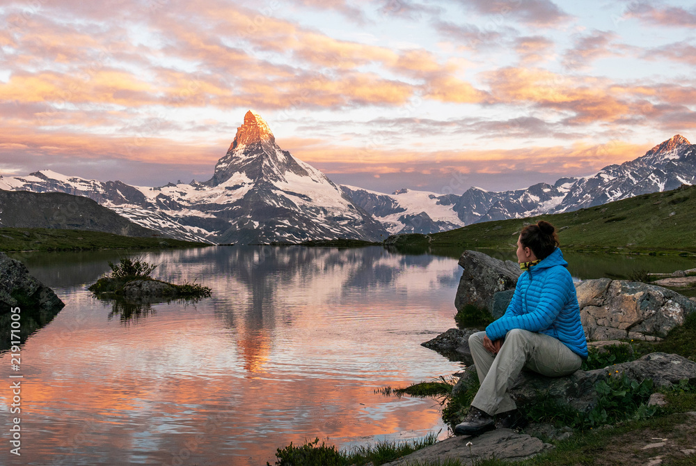 Obraz premium Morning shot of the golden Matterhorn (Monte Cervino, Mont Cervin) pyramid and blue Stellisee lake. Female tourist enjoying view of early morning Matterhorn mountain is Valais Alps, Switzerland.