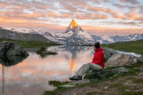Morning shot of the golden Matterhorn (Monte Cervino, Mont Cervin) pyramid and  blue Stellisee lake. Female tourist enjoying view of early morning Matterhorn mountain is Valais Alps, Switzerland.