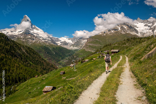 Female traveler with backpack hiking mountain trail and admiring views of Majestic Matterhorn mountain in Valais (Pennine) Alps, Switzerland.
