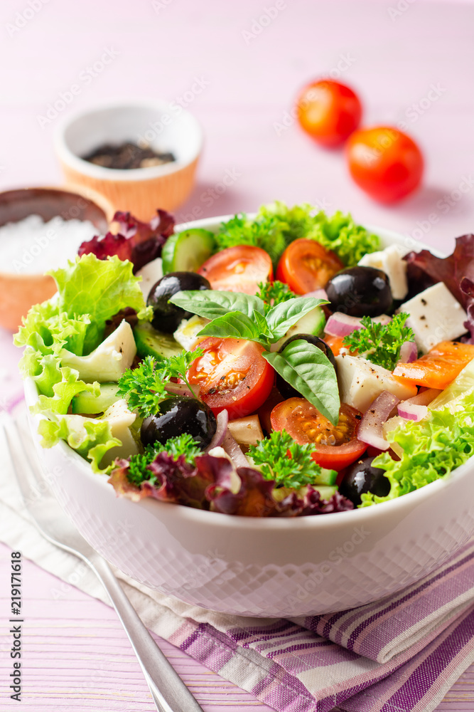 Fresh Greek salad with vegetables, feta cheese and black olives in white bowl on purple wooden background Fresh Greek salad with vegetables, feta cheese and black olives in white bowl on purple wooden background