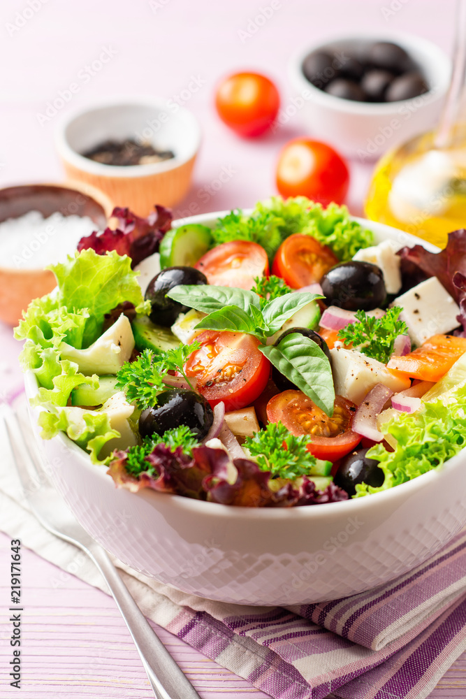 Fresh Greek salad with vegetables, feta cheese and black olives in white bowl on purple wooden background
