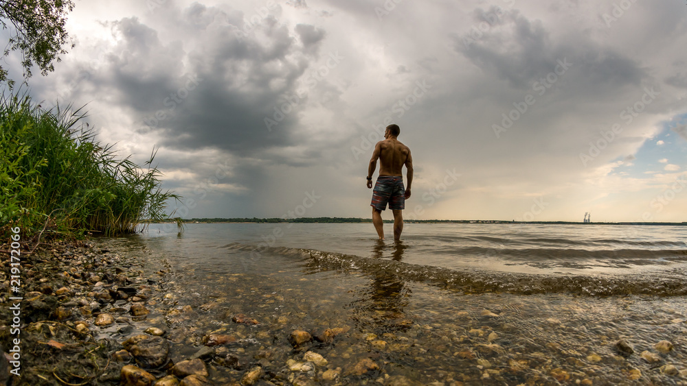 Trainierter Mann geht in einen See zum Schwimmen bei heranziehendem Unwetter