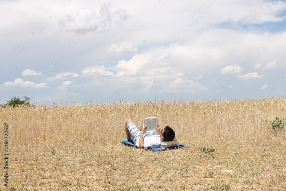 Obraz premium Chico joven leyendo un libro en el campo con nubes