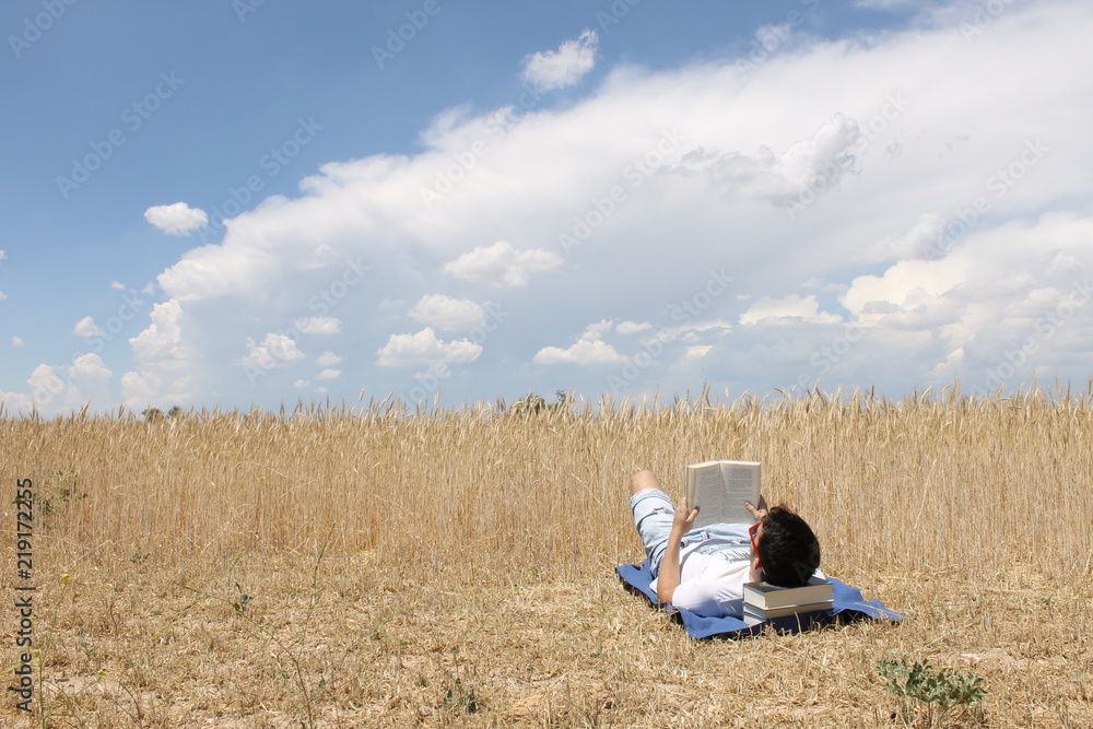 Chico joven leyendo un libro en el campo con nubes Chico joven leyendo un libro en el campo con nubes